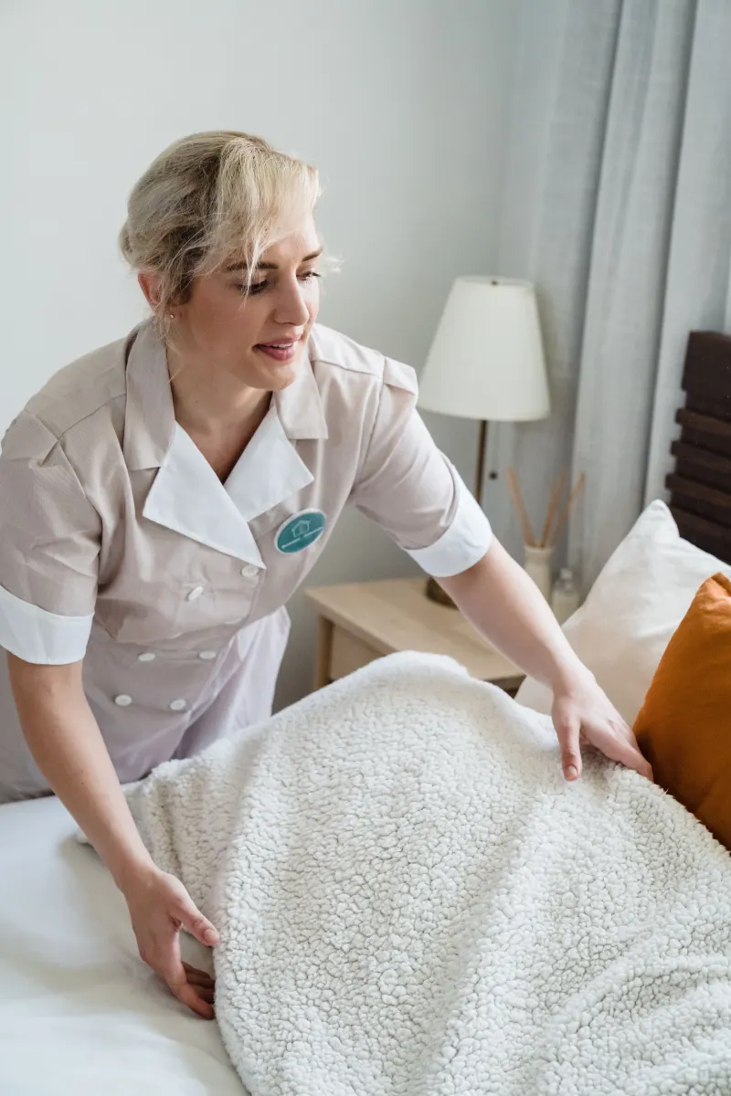 A carer makes a bed with a soft blanket in a bright bedroom